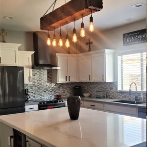May include: A rustic wooden kitchen island light fixture with eight Edison bulbs hanging from black chains. The light fixture is suspended from a wooden beam.