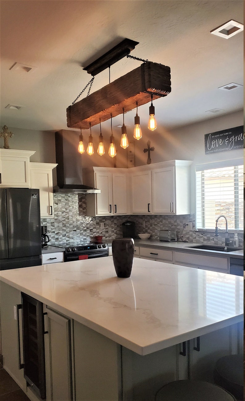 May include: A rustic wooden kitchen island light fixture with eight Edison bulbs hanging from black chains. The light fixture is suspended from a wooden beam.