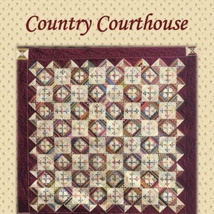 May include: A quilted textile with a burgundy border and a repeating diamond pattern. The quilt features a variety of colors within the diamond shapes, including blue, green, and red. The text "Country Courthouse" is at the top.