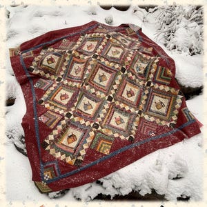 May include: A handmade quilt with a burgundy border and a repeating pattern of small houses in squares. The quilt is on a snowy surface, with the text "Calico Cottages" and "Sew'n Wild Oaks" visible.