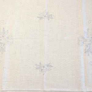 May include: Cream-colored linen tablecloth with embroidered floral designs in a light blue hue. The embroidery features detailed depictions of flowers and foliage, arranged in a symmetrical pattern across the fabric.