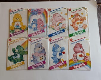 May include: A collection of vintage Butterick sewing patterns featuring Care Bears. Each pattern cover displays a different bear character with its name, such as "Birthday Bear" and "Grumpy Bear", and a rainbow.