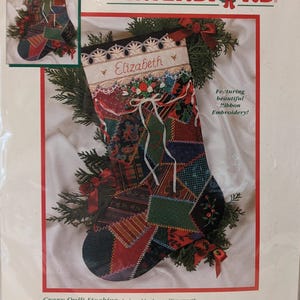 May include: A Dimensions 16-inch Crazy Quilt Stocking embroidery kit package featuring a patchwork-style Christmas stocking with ribbon embroidery, a white cuff with the name Elizabeth, and various fabric patterns in red, green, and dark blue.