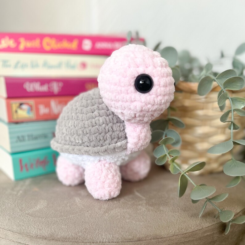 K&ouml;nnte beinhalten: Ein geh&auml;keltes rosa und graues Schildkr&ouml;tenspielzeug mit schwarzen Augen. Die Schildkr&ouml;te sitzt auf einer hellgrauen Oberfl&auml;che.