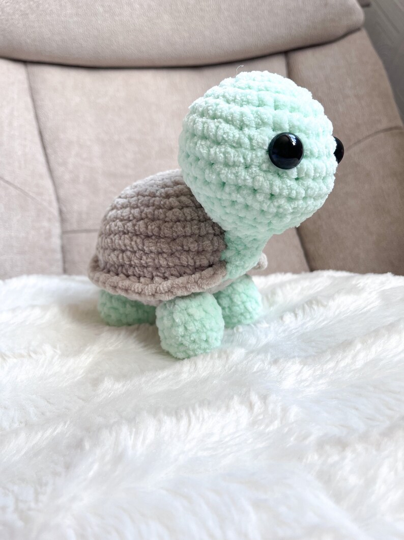 K&ouml;nnte beinhalten: Ein geh&auml;keltes Schildkr&ouml;tenspielzeug mit einer hellgr&uuml;nen Schale und einem braunen Unterleib. Das Spielzeug hat gro&szlig;e schwarze Augen und eine weiche, flauschige Textur.