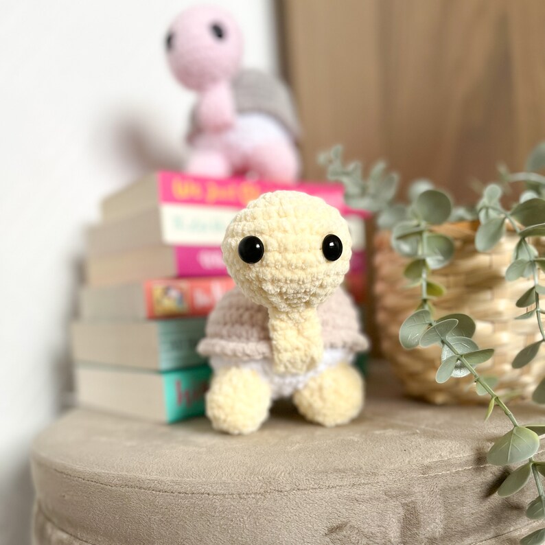 K&ouml;nnte beinhalten: Ein geh&auml;keltes Schildkr&ouml;tenspielzeug mit einer cremefarbenen Schale und einer hellrosa Unterseite. Die Schildkr&ouml;te hat schwarze Augen und sitzt auf einer beigefarbenen Oberfl&auml;che.