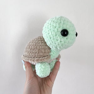 K&ouml;nnte beinhalten: Ein geh&auml;keltes gr&uuml;nes und braunes Pl&uuml;schtier in Form einer Schildkr&ouml;te mit schwarzen Augen.