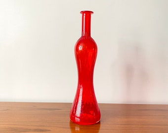 May include: A tall, vibrant red glass vase featuring a slender, elongated neck that transitions into a wider, bulbous midsection and a flared, circular base. The glass is translucent, allowing light to pass through its smooth, polished surface.