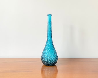 Peut inclure: Un grand vase en verre bleu élancé avec un col étroit et une base bulbeuse. Toute la surface du vase présente une texture circulaire en relief distincte, créant un aspect alvéolé et tactile sur l'ensemble du verre bleu translucide.