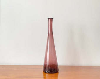 May include: A tall, slender, conical glass vase in a translucent mauve purple hue. The vase features a wide, circular base that tapers upwards into a narrow, elongated neck with a simple, smooth rim at the top, showcasing a clean, minimalist form.