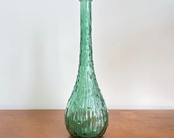 May include: A tall, slender green glass vase with a narrow neck and a bulbous base. The surface of the glass features a distinct vertical ribbed texture with small, raised bumps throughout, creating a tactile, organic appearance across the body.