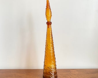 May include: A tall, amber-colored glass decanter with a conical shape and a matching pointed stopper. The surface of the glass features a raised, swirling wave-like texture that extends from the base up to the top of the stopper.