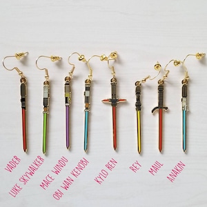 Puede incluir: Nueve pares de pendientes de sable de luz dorados con hojas de diferentes colores. Las hojas de los sables de luz son rojas, amarillas, verdes, azules, moradas, negras y blancas. Los pendientes est&aacute;n etiquetados con los nombres de los personajes de Star Wars: Vader, Luke Skywalker, Mace Windu, Obi Wan Kenobi, Kylo Ren, Rey, Maul y Anakin.