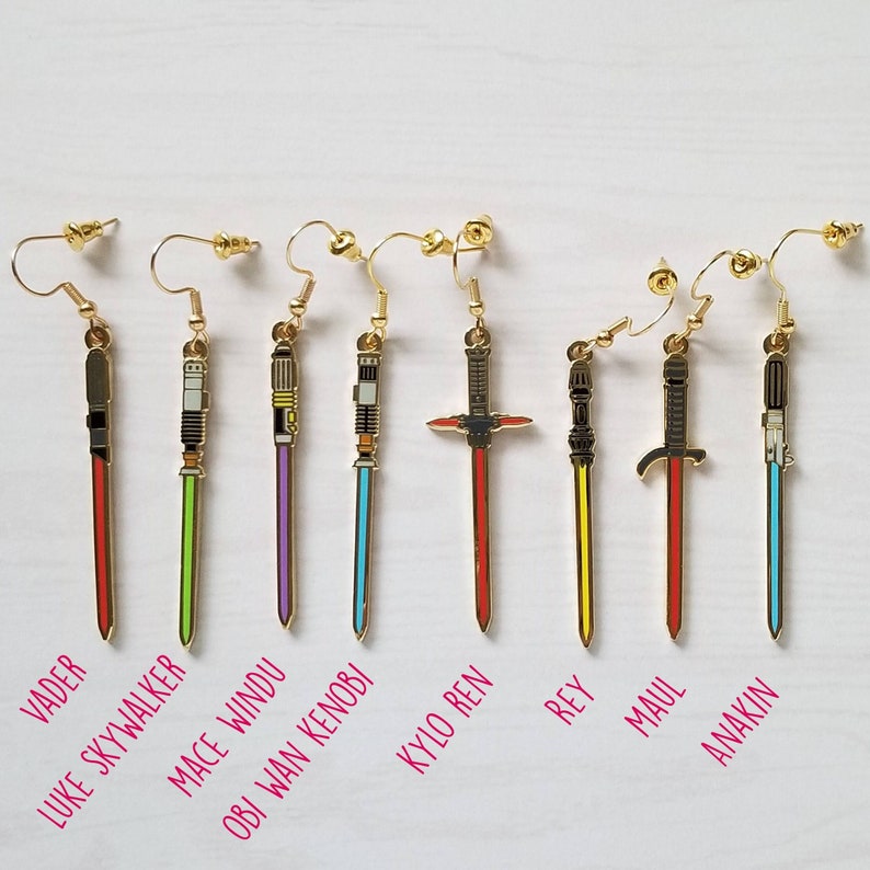 Puede incluir: Nueve pares de pendientes de sable de luz dorados con hojas de diferentes colores. Las hojas de los sables de luz son rojas, amarillas, verdes, azules, moradas, negras y blancas. Los pendientes est&aacute;n etiquetados con los nombres de los personajes de Star Wars: Vader, Luke Skywalker, Mace Windu, Obi Wan Kenobi, Kylo Ren, Rey, Maul y Anakin.