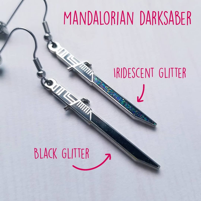Puede incluir: Un par de pendientes de plata con forma de sable oscuro mandaloriano. Un pendiente tiene purpurina negra y el otro tiene purpurina iridiscente.