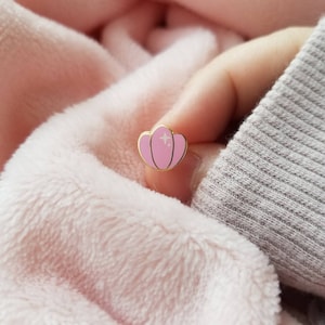 May include: A pink enamel pin shaped like a seashell with gold accents and white glitter details.