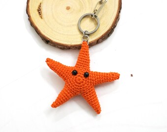 May include: Orange crocheted starfish keychain with black eyes. The starfish is attached to a silver key ring.