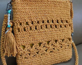 Puede incluir: Un bolso de hombro de crochet marrón con una borla y una correa de cuentas. El bolso tiene un patrón floral y está hecho con un hilo grueso.