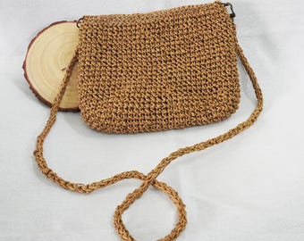 Könnte beinhalten: Eine braune geflochtene Strohtasche mit einem langen Schulterriemen. Die Tasche ist aus einem dicht gewebten Strohmaterial gefertigt und hat ein schlichtes, klassisches Design.