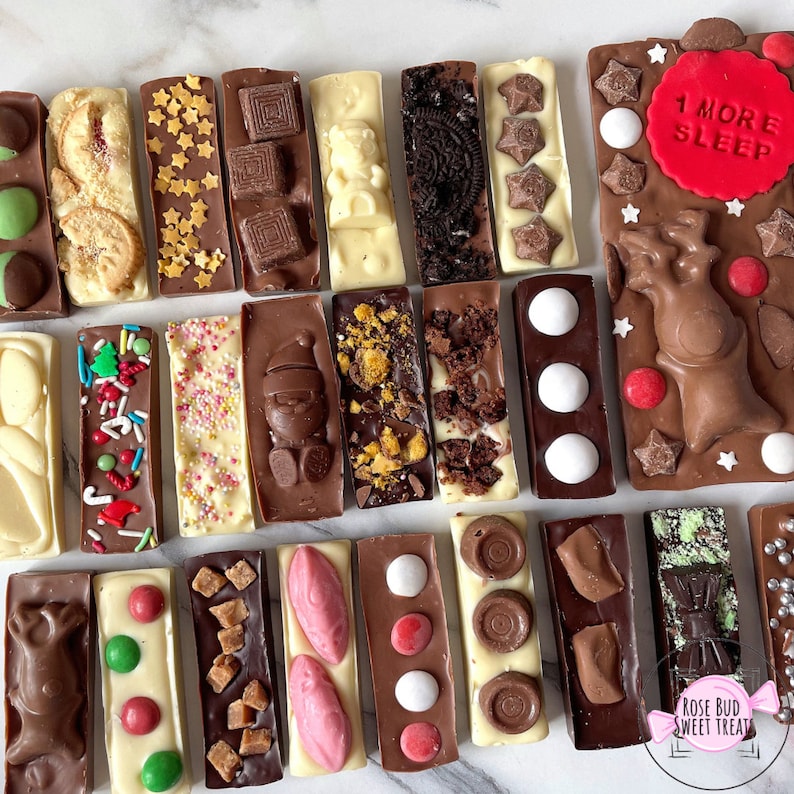May include: An assortment of decorative chocolate bars with various toppings, including cookies, sprinkles, and festive shapes. Some bars feature holiday-themed designs, and one has the text "1 MORE SLEEP" on a red background.