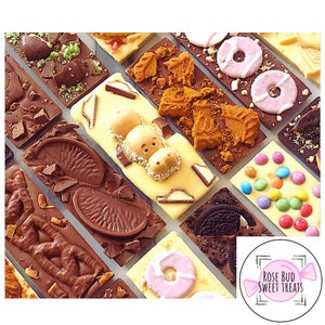 May include: Assortment of chocolate bars with various toppings, including Oreos, Smarties, and fruit slices. The bars are arranged in a grid pattern and are all different colors and shapes. The text "Rose Bud Sweet Treats" is visible in the lower right corner of the image.
