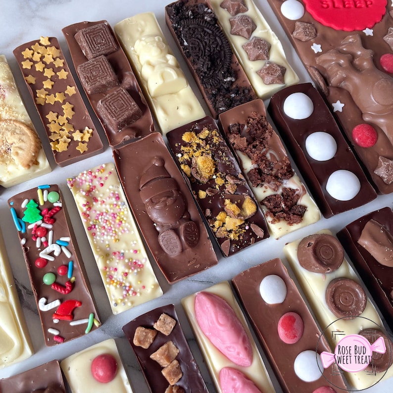 May include: An assortment of chocolate bars with various toppings, including stars, sprinkles, cookies, and candies. The bars are in milk, dark, and white chocolate. Some bars have festive decorations, and one has the word "SLEEP" on it.