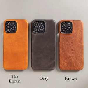 May include: Three leather phone cases in tan, gray, and brown. The cases are designed for an iPhone.
