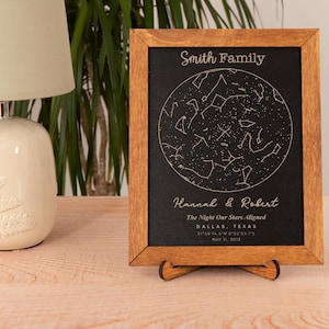 May include: A wooden framed print with a black background featuring a constellation map with gold stars. The text "Smith Family", "Hannah & Robert", "The Night Our Stars Aligned", "Dallas, Texas", and "May 11, 2013" is printed in gold.