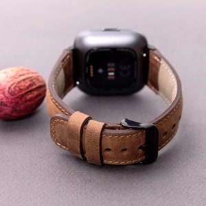 May include: A brown leather watch band with a black buckle. The band is designed for a square-shaped smartwatch.