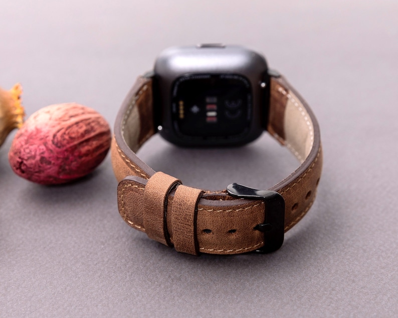 May include: A brown leather watch band with a black buckle. The band is designed for a square-shaped smartwatch.