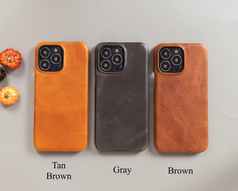 May include: Three leather phone cases in tan, gray, and brown. The cases are designed for an iPhone.