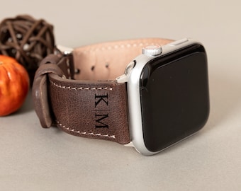 May include: A brown leather watch strap with the initials "KIM" engraved on it. The strap is attached to a silver Apple Watch.
