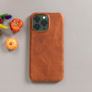 May include: A brown leather phone case with a green camera lens cutout. The case has a textured surface.