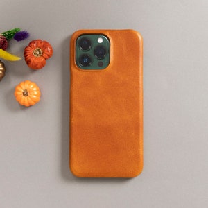 May include: A brown leather phone case for an iPhone with a camera cutout. The case has a textured surface.