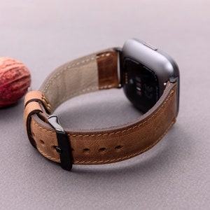 May include: A brown leather watch band with a black buckle. The band is designed for a smartwatch with a square face.