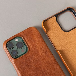 May include: A brown leather phone case with a camera cutout. The case has a textured surface and a dark brown color.