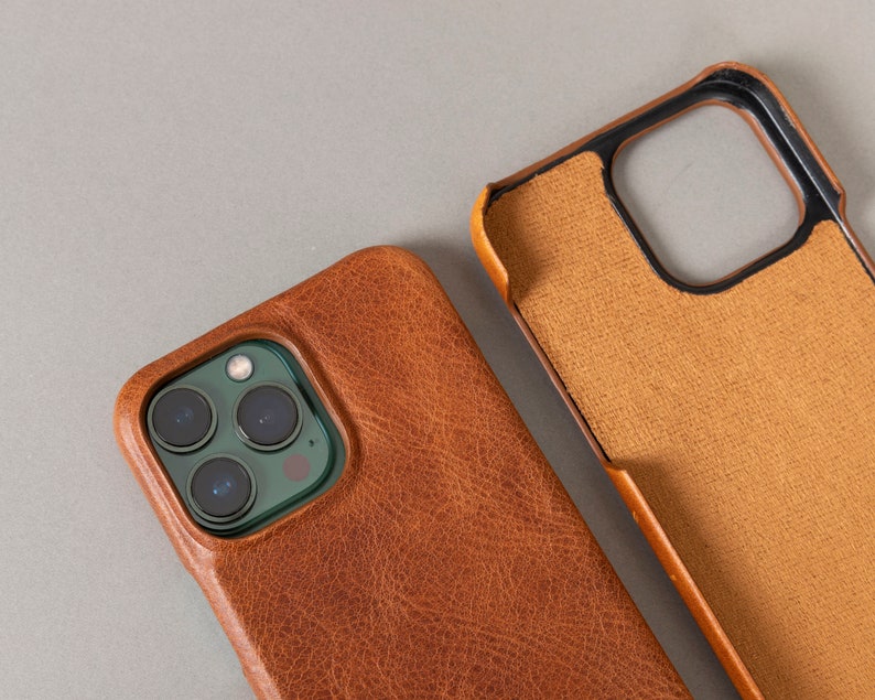 May include: A brown leather phone case with a camera cutout. The case has a textured surface and a dark brown color.
