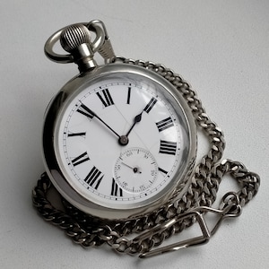 May include: A silver pocket watch with a white face and black Roman numeral hour markers. The watch has a silver chain attached to it.