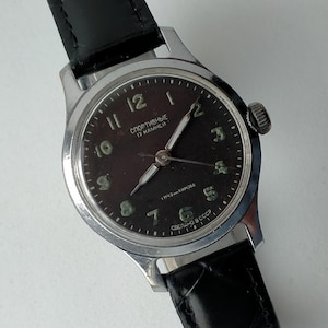 May include: A black-faced wristwatch with silver accents. The watch face has white numerals and a black second hand. The watch face also has the text "СПОРТИВНЫЕ 17 КАМНЕЙ" and "1 МЧЗ КИРОВА" and "СДЕЛАНО В СССР".