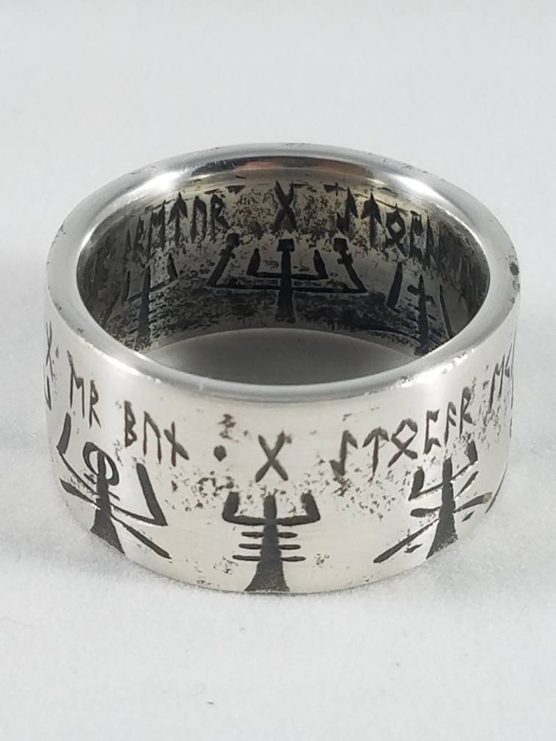 May include: A silver ring with a black inscription and symbols. The inscription reads "MR. BNX. X. STRCFR".