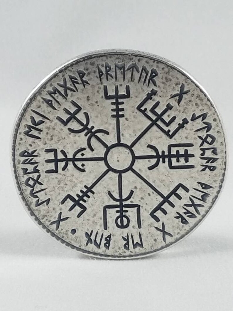 May include: A silver-colored circular pendant with a black compass design and runes around the edge. The runes read "MR. BIX. X.  SVEA.  R.  PMTAR.  X.  SMAR.  A.  VIX.  X.  MR.  BIX."