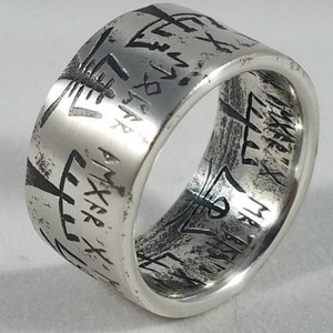 May include: A silver ring with a wide band and intricate engraved designs. The band is textured and has a worn look.