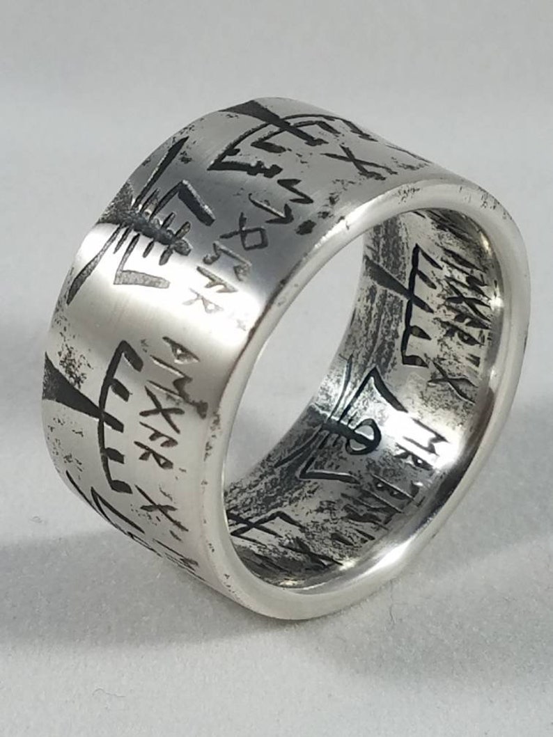 May include: A silver ring with a wide band and intricate engraved designs. The band is textured and has a worn look.