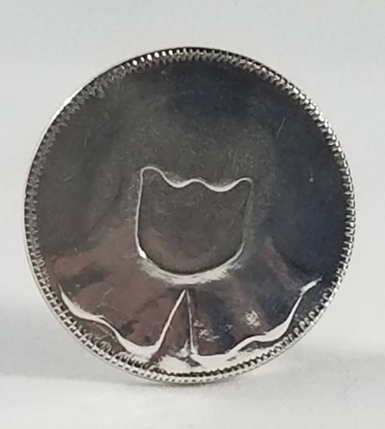 K&ouml;nnte beinhalten: Silberfarbener Metall-Token mit einem stilisierten Tulpenmotiv.