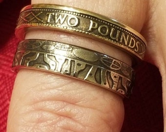 May include: Two gold rings made from coins. The top ring has the words "TWO POUNDS" engraved on it. The bottom ring has a more intricate design.