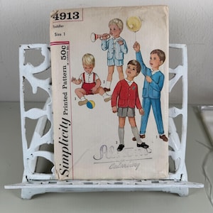May include: Vintage Simplicity toddler pattern, size 1, featuring illustrations of young boys in various outfits. The pattern is held in a white, ornate metal stand. The pattern's price is 50c.