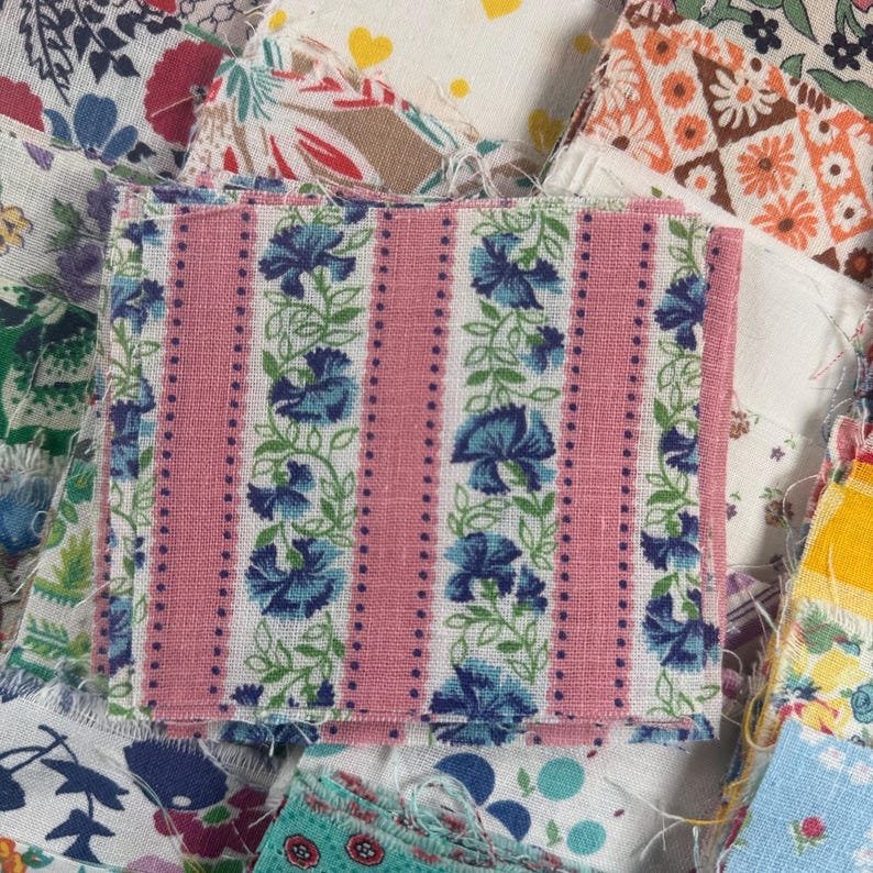 May include: A square fabric patch with a pink striped background and vertical rows of blue floral patterns. The patch is surrounded by other fabric pieces with various floral and geometric designs.