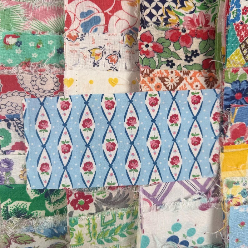 May include: Close-up of a patchwork quilt with various fabric patterns. A light blue fabric with a white polka dot background and a repeating pattern of pink roses and white diamond shapes is featured prominently. Other fabrics include floral and geometric designs.
