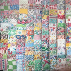 May include: A patchwork quilt composed of numerous fabric squares in various colors and patterns. The quilt features a mix of floral, geometric, and abstract designs in shades of pink, blue, green, yellow, and red. The squares are arranged in a grid-like pattern.