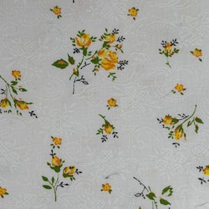 Könnte beinhalten: Weißer Stoff mit einem sich wiederholenden Muster aus gelben Rosen und grünen Blättern. Die Rosen haben orangefarbene Zentren. Der Hintergrund hat ein subtiles, geprägtes Blumenmuster.
